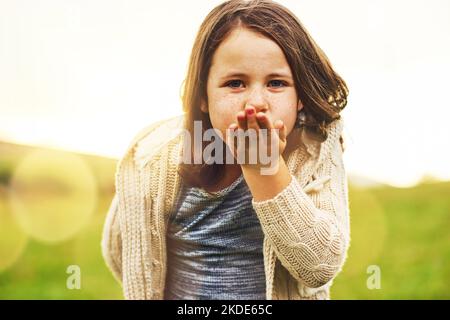 Küsse kommen dir zu. Porträt eines süßen kleinen Mädchens, das draußen einen Kuss bläst. Stockfoto