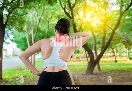 Lauffrau mit Schultermuskelschmerzen in einem Park. Konzept der Schulterschmerzen eines Läufers. Athlet Mädchen in Schmerzen reiben ihre Schulter im Freien. Stockfoto