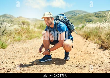 Ein junger Mann schnürte sich seine Schnürsenkel, während er auf einer Wanderung unterwegs war. Stockfoto