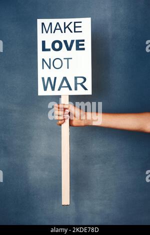 Frieden ist der einzige Weg. Studioaufnahme einer Frau mit einem Schild, auf dem steht, dass Liebe nicht Krieg gegen einen blauen Hintergrund führt. Stockfoto