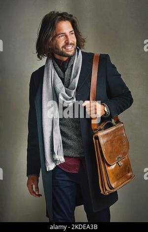 Mode bevorzugt die Kühnen. Ein stilvoll gekleideter Mann posiert mit einer Ledertasche im Studio. Stockfoto