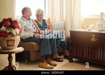 In den Silberjahren auf dem neuesten Stand. Ein Seniorenpaar, das zu Hause einen Laptop auf dem Sofa zusammen benutzt. Stockfoto