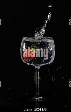 Erdbeere fiel in ein Weinglas mit Wasser mit Spritzer auf schwarzem Hintergrund Stockfoto