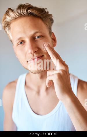 Ich kümmere mich um meine Haut. Porträt eines jungen Mannes, der zu Hause Feuchtigkeitscreme auf sein Gesicht anwendet. Stockfoto