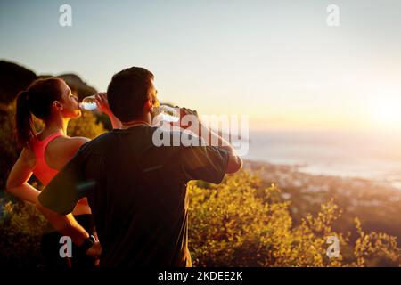 Abkühlung mit Aussicht. Ein sportliches junges Paar, das eine Pause einlegt, während es gemeinsam auf einen Lauf geht. Stockfoto