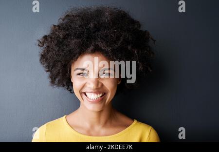 Ihr bestes Lächeln auf den Lippen. Studioportrait einer attraktiven jungen Frau, die vor grauem Hintergrund posiert. Stockfoto