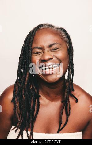 Fröhliche Frau lächelt fröhlich mit einer Kapsel Omega-3-Fettsäuren zwischen ihren Zähnen. Reife Frau mit Dreadlocks mit Nahrungsergänzungsmitteln als Stockfoto