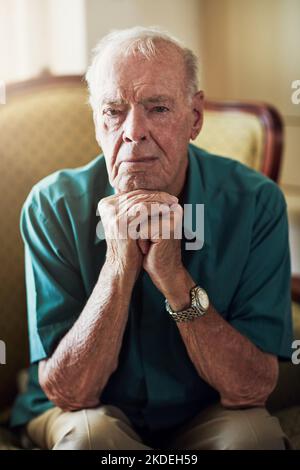 Ich bin jetzt alle zerknittert und mürrisch. Beschnittenes Porträt eines älteren Mannes, der mit den Händen auf dem Kinn in einem Wohnzimmer sitzt. Stockfoto