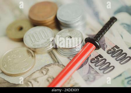 Japanischer Yen in Banknoten und Münzen und eine Miniatur-Katana in roter Scheide. Stockfoto