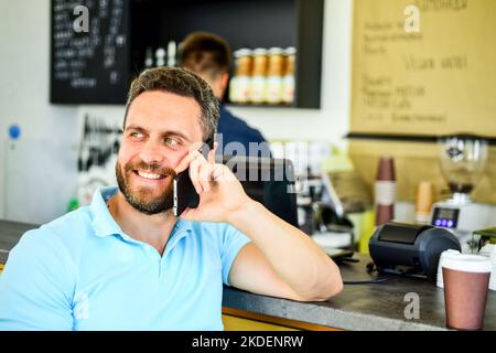 Mann mit Smartphone bestellt Kaffee. Kaffeepause-Konzept. Treffen wir uns im Café. Mann mobile Gespräch Café Barista Hintergrund. Trinken Sie Kaffee, während Sie warten Stockfoto