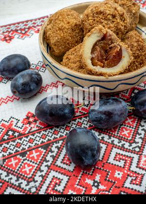 Süße Pflaumenknödel aus gesäuertem Teig und frische Pflaumen auf Tonschüssel und Pflaumen zur Seite Stockfoto