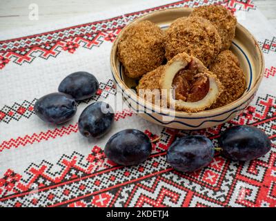 Süße Pflaumenknödel aus gesäuertem Teig und frische Pflaumen auf Tonschüssel und Pflaumen zur Seite Stockfoto