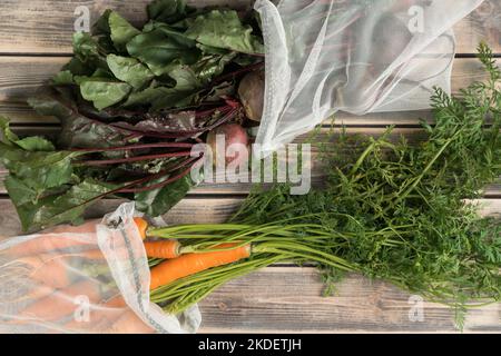 Trauben von frischen Rüben und Karotten mit langem grünem Schleppen auf Holztisch, Draufsicht. Auspacken von Bauerngemüse aus Öko-Stoffsäcken. Bio-Lebensmittel oder er Stockfoto