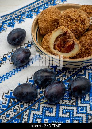 Süße Pflaumenknödel aus gesäuertem Teig und frische Pflaumen auf Tonschüssel und Pflaumen zur Seite Stockfoto