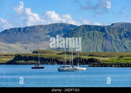 Boote, die im Hafen von Canna mit den Inseln Sanday und Rum vor Anker liegen. Von der Isle of Canna, Schottland, Großbritannien. Stockfoto