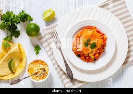 Vegetarische Enchilada-Kasserolle mit Tortillas, Sauce, Pinto-Bohnen, Mais, Zucchini und mexikanischem Käse auf weißem Teller, flacher Laie Stockfoto