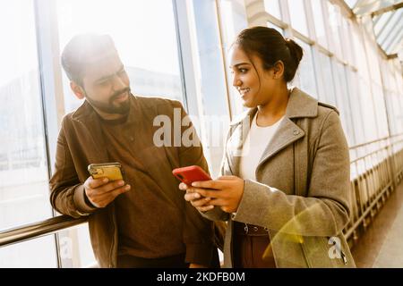 Indisches Paar, das im Flughafengebäude spricht und Mobiltelefone benutzt Stockfoto