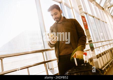 Indischer bärtiger Mann, der in Innenräumen am Bahnhof ein Mobiltelefon benutzte Stockfoto