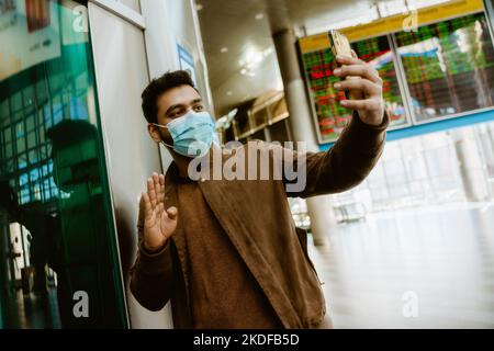 Indischer Mann mit Gesichtsmaske, der Selfie auf dem Handy im Bahnhof im Haus nimmt Stockfoto