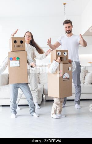 Fröhliche Familie von Eltern und zwei Kindern, die zu Hause tanzen wie Roboter, Kinder tragen handgefertigte Moving-Box-Kostüme aus Pappe Stockfoto