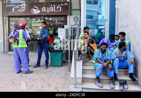 KATAR, Doha, Musheireb, Bauboom für FIFA Fußball WM 2022, der Bau wird von Wanderarbeitern aus aller Welt durchgeführt, Mittagspause unterwegs / KATAR, Doha, Bauboom fuer die FIFA Fußball WM 2022 / KATAR, Doha, Bauboom fuer die FIFA Fußball WM 2022, Abrissviertel Musheireb, auf den Baustellen für Neubauten schufen Gastarbeiter aus aller Welt, Workers at Mittagspause auf der Strasse Stockfoto