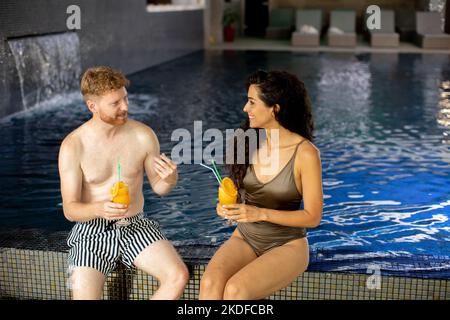 Schönes junges Paar, das sich entspannt und frischen Orangensaft am Pool trinkt Stockfoto