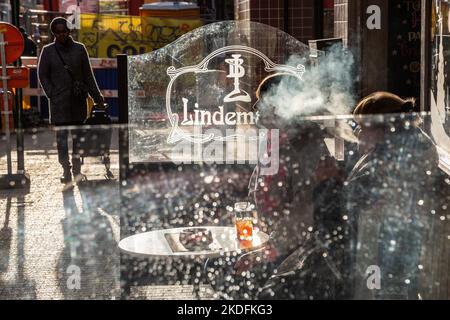 Zwei Damen, eine davon rauchend, sitzen an einem sonnigen Wintertag vor einem Café und haben eine Hintergrundbeleuchtung. Brüssel. Stockfoto