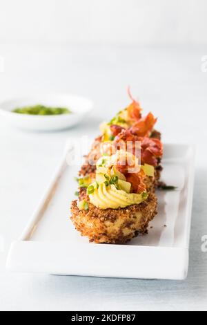 Eine Reihe frittierter, devilierter Eier auf einer weißen Platte, garniert mit Schnittlauch. Stockfoto