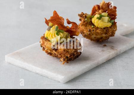 Zwei frittierte, deviled Egg-Vorspeisen auf einer weißen Marmorplatte. Stockfoto