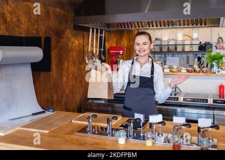 Kellnerin serviert dem Gast Essen zum Mitnehmen an der Theke in einem kleinen Familienrestaurant. Stockfoto