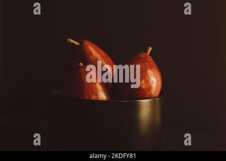 Rote Birnen in einer schwarzen Obstschale auf dunklem Hintergrund Stockfoto