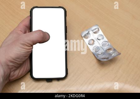 Blick auf ein Smartphone mit einem isolierten weißen Bildschirm in der Hand einer Person vor dem Hintergrund eines Tisches Stockfoto