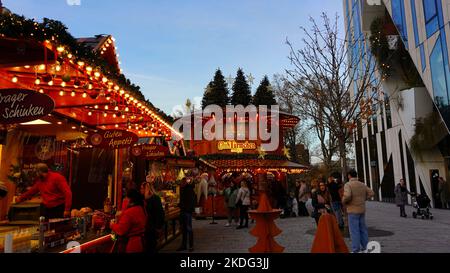 Traditioneller Weihnachtsmarkt steht auf dem Weihnachtsmarkt 2021 in Düsseldorf neben moderner Architektur des Kö-Bogen von Daniel Libeskind. Stockfoto