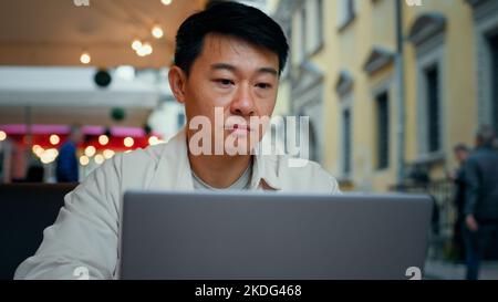 Nahaufnahme asiatischer Mann sitzt im Café tippt auf Laptop chatten online lesen gute Nachricht männlich Tourist browses Social Network wählt Hotel im Internet Stockfoto