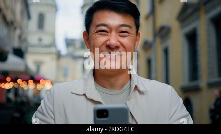 Zufriedener Mann Kunde im Freien stehend hält Handy Blick auf Kamera genießt Internet-Shopping auf Smartphone im Online-Shop freudig Stockfoto