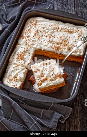 Kürbiskuchen mit Cremezuckerguss in Backform und einer Scheibe auf einer Kuchenschaufel, vertikale Ansicht von oben Stockfoto