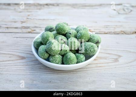 Wasabi-Nüsse liegen in einer weißen Porzellanschale auf einer Holzoberfläche Stockfoto