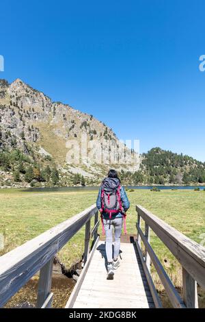 Frau, die auf einer Holzbrücke mit dem Laurenti-See im Hintergrund, Ariege, Pyrenäen, Frankreich, geht Stockfoto