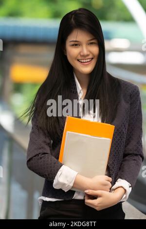 Junge asiatische Frau mit Büchern und lächelnd Blick auf die Kamera in der Universität, Menschen Bildungskonzept. Stockfoto
