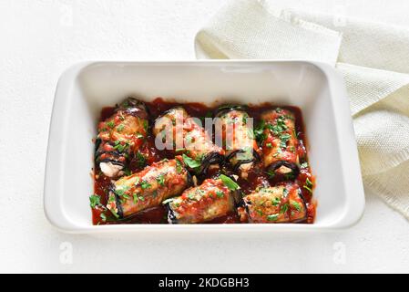 Gebackene gefüllte Auberginen-Brötchen mit Tomatensauce in Backform auf weißem Hintergrund. Nahaufnahme Stockfoto