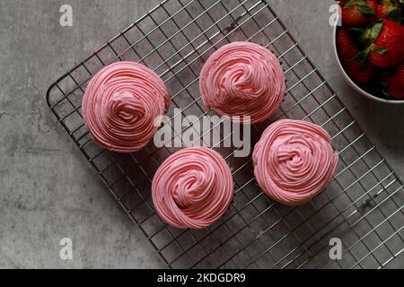 Blick von oben auf Muffins mit rosafarbenem Buttercreme-Zuckerguss auf dem grauen Marmortisch Stockfoto