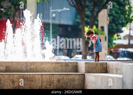 Schwarzes brasilianisches Kleinkind, das den Savassi-Brunnen in Belo Horizonte, Brasilien, ansieht. Stockfoto