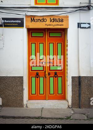 Jerico, Antioquia, Kolumbien - 3 2022. April: Grüne und orangefarbene Tür auf weißem Hintergrund, mit einem Schild mit der Aufschrift „Schreibwaren und Sublimation“ Stockfoto