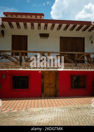 Jerico, Antioquia, Kolumbien - April 5 2022: Weißes und rotes Kolonialhaus mit Holzbalkon gegen blauen Himmel Stockfoto