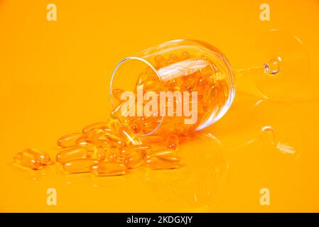 Fischöl-Kapseln. Gelbe Omega 3 Pillen im Glas auf den gelben und orangen Fischöl Kapseln im Glas . im Glas. In Eimer Ampullen. Isoliert auf gelbem und Stockfoto