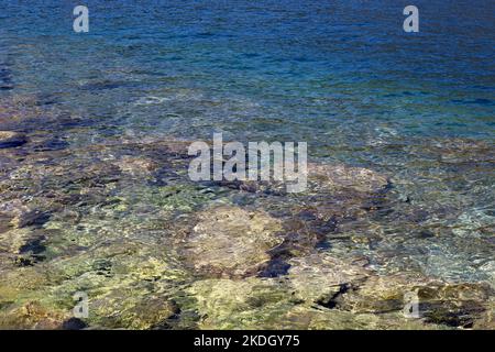 Die durchsichtige Oberfläche des Meeres mit den Steinen auf dem Grund. Felsiger Strand, türkisfarbenes Wasser als Hintergrund Stockfoto