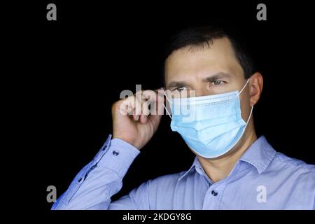 Porträt des weißen Mannes in Schutzmaske auf schwarzem Hintergrund. Sicherheit während einer Coronavirus-Pandemie Stockfoto