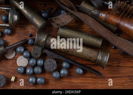 Antike 16-Gauge Break-Action glatt gebohrte Schrotflinte mit Messinggehäuse und Zubehör für Patronennachladung auf Holztisch. Stockfoto