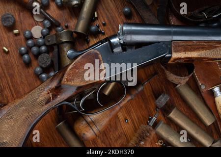 Antike 16-Gauge Break-Action glatt gebohrte Schrotflinte mit Messinggehäuse und Zubehör für Patronennachladung auf Holztisch. Stockfoto