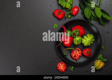 Grüne und rote gerippte Tomaten, amerikanische oder florentinische Sorte. Reifes Gemüse, Chili, frische Lorbeerblätter. Trendiges hartes Licht, dunkler Schatten, Steinbeton Stockfoto